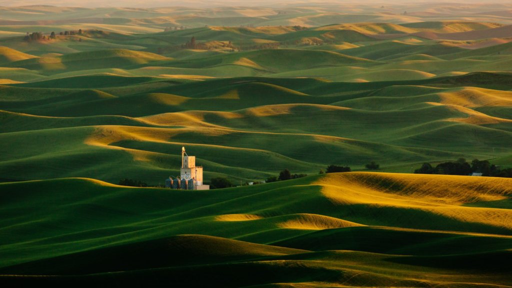 large green field with hills and several silos in the distance